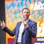 Eric Trump presenting at Bitcoin conference with Bitcoin symbol and financial charts representing institutional demand and supply scarcity.