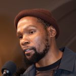 A close-up photo of NBA star Kevin Durant speaking into a microphone. The image is used in an article discussing his accidental, massive gains on a Bitcoin investment after being locked out of his Coinbase account.