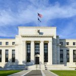 Bitcoin coin in front of the U.S. Federal Reserve building symbolizing potential market impact of next Fed chair.