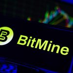 A smartphone displays the logo for BitMine, a digital asset company. In the background, a financial chart is visible, representing the market volatility referenced in the October 2025 article about BitMine's large Ether acquisition post-crash.