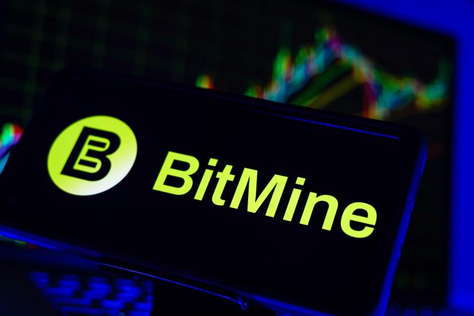 A smartphone displays the logo for BitMine, a digital asset company. In the background, a financial chart is visible, representing the market volatility referenced in the October 2025 article about BitMine's large Ether acquisition post-crash.