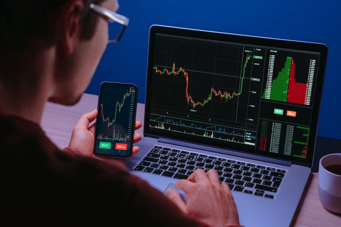 A crypto trader analyzes financial charts on both a laptop and a smartphone, where "BUY" and "SELL" buttons are visible. The image represents the active analysis of market data as the October 2025 article discusses the divergent performance and bullish sentiment for cryptocurrencies like XRP and Solana compared to Bitcoin and Ether.