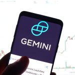 A smartphone displays the logo for the Gemini cryptocurrency exchange. In the background, a blurred financial chart is visible, representing the market analysis of crypto exchange stocks mentioned in the October 2025 article, which details Citi's price target cut for Gemini (GEMI) due to slowing volume.