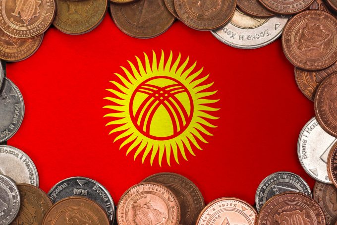 The flag of Kyrgyzstan is framed by a border of various international coins. This image represents the nation's financial system and currency (the Som), relevant to the October 2025 article about Kyrgyzstan launching a Som-pegged stablecoin and accelerating its Central Bank Digital Currency (CBDC) pilot.