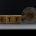 Wooden blocks spelling "ETF" stand next to a physical Ripple (XRP) coin.