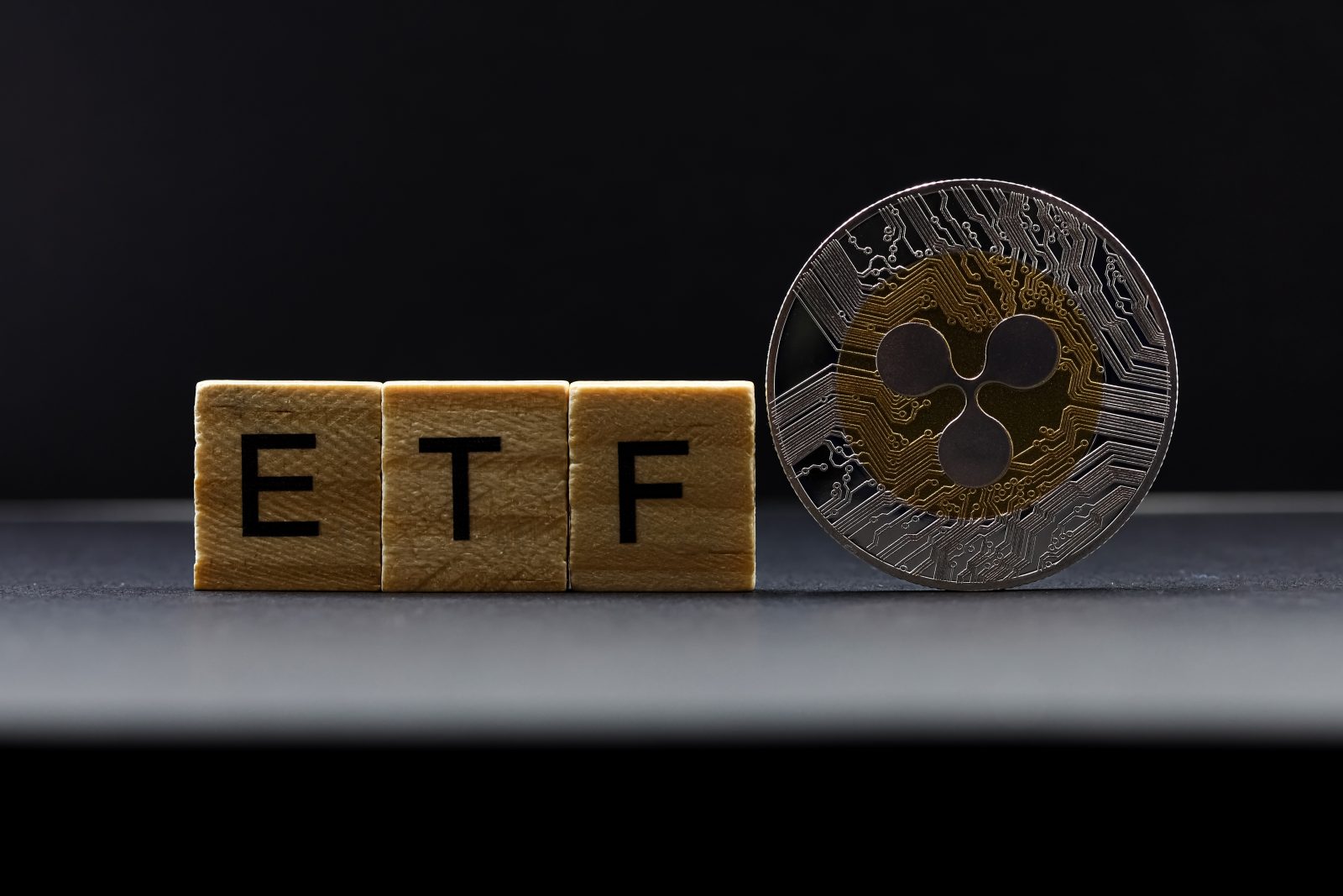 Wooden blocks spelling "ETF" stand next to a physical Ripple (XRP) coin.