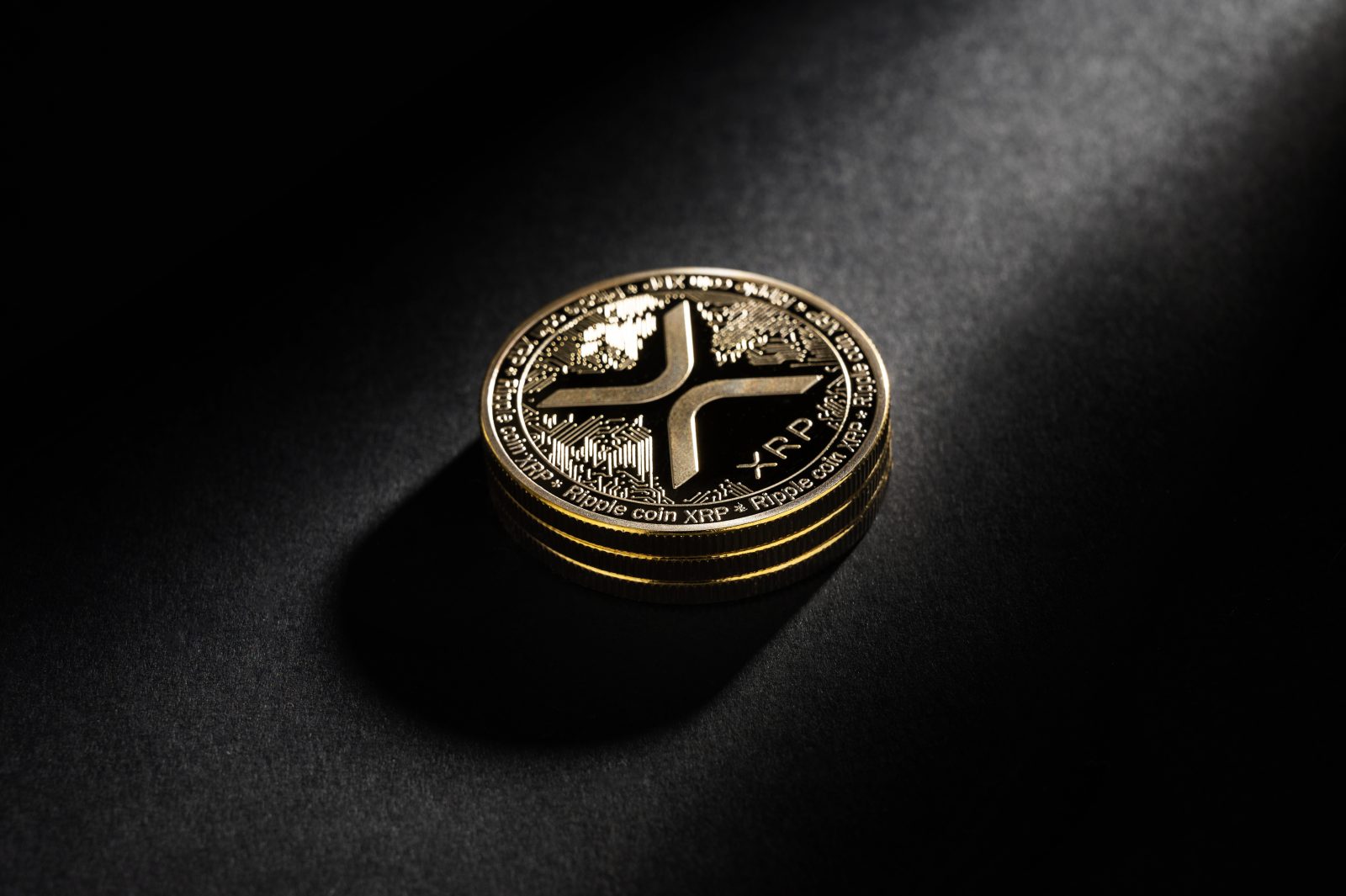 A physical Ripple (XRP) coin is shown in a dramatic spotlight on a dark background.
