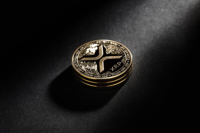 A physical Ripple (XRP) coin is shown in a dramatic spotlight on a dark background.