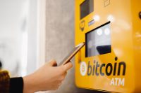 A user interacting with a bright yellow Bitcoin ATM using a smartphone.