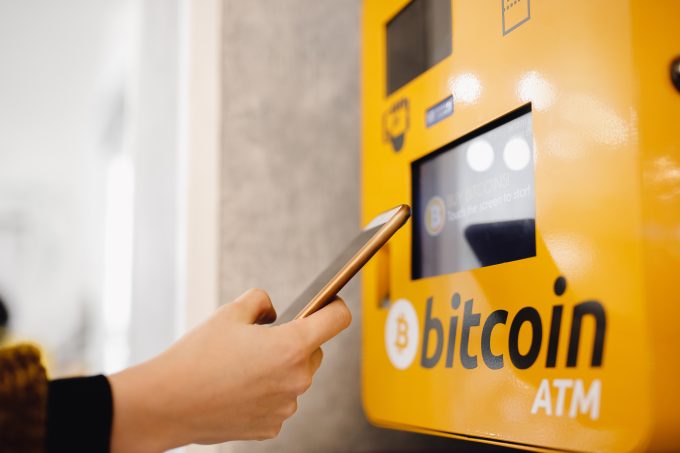A user interacting with a bright yellow Bitcoin ATM using a smartphone.