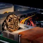 A physical gold Bitcoin coin rests on the internal heatsink of a computer, symbolizing cryptocurrency mining.