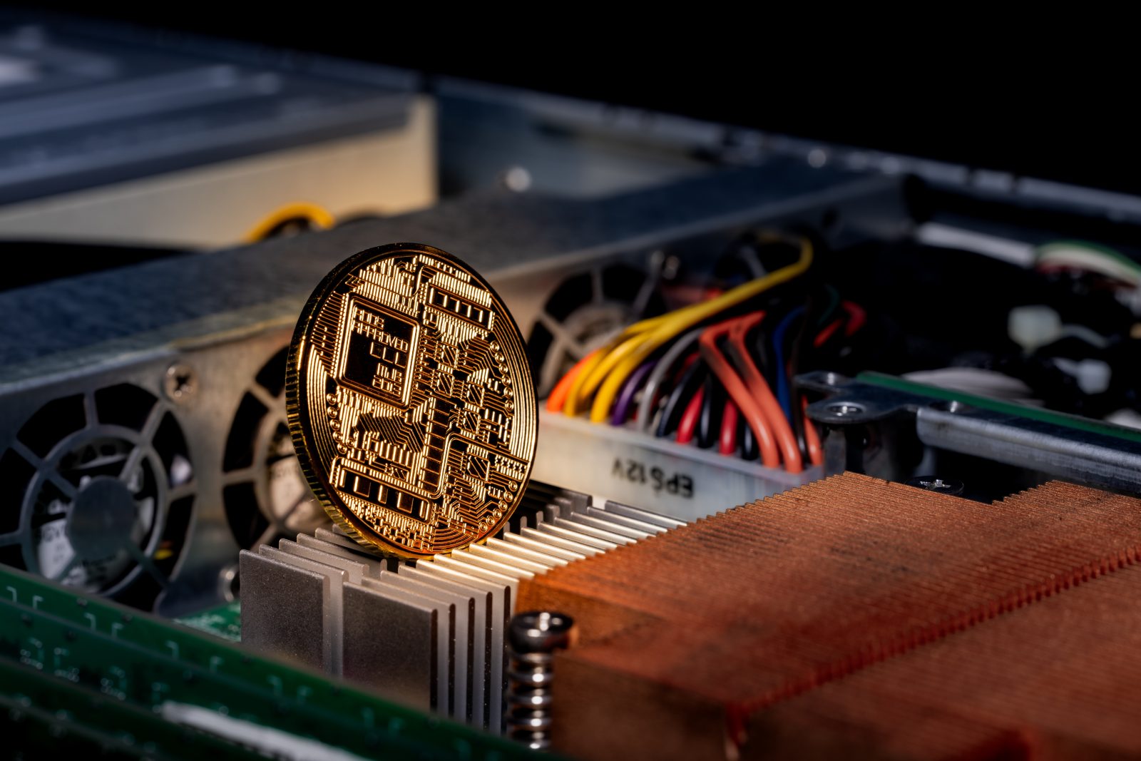 A physical gold Bitcoin coin rests on the internal heatsink of a computer, symbolizing cryptocurrency mining.