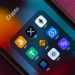A close-up of a smartphone screen showing a 'Crypto' folder with app icons for various cryptocurrencies, including XRP and Solana (SOL).