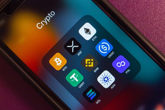 A close-up of a smartphone screen showing a 'Crypto' folder with app icons for various cryptocurrencies, including XRP and Solana (SOL).